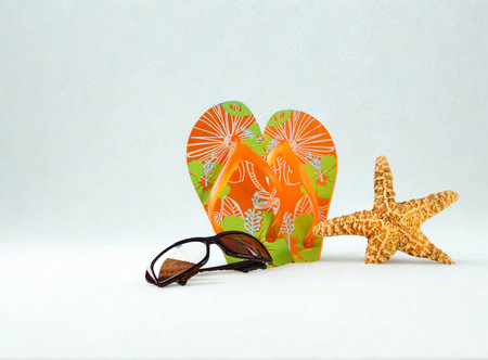 A pair of colorful flip flops rests next to sunglasses and a starfish on a plain white background.の写真素材