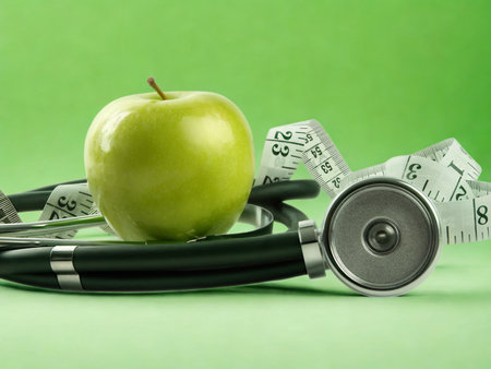A green apple, stethoscope, and measuring tape are arranged on a green background, symbolizing health and wellness.の写真素材