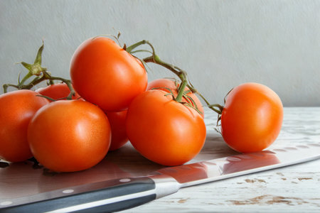 A cluster of ripe, red tomatoes rests on a wooden cutting board next to a kitchen knife.の写真素材