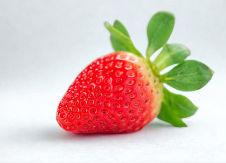 A close-up studio shot of a single, bright red, ripe strawberry with vibrant green leaves against a...