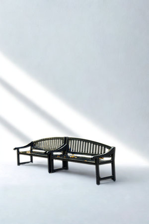 Two dark curved wooden park benches are arranged in an L-shape, casting shadows on a bright white surface with diagonal light streaks.の写真素材