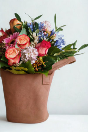 A colorful bouquet of roses, daisies, and other blooms is presented in a simple, textured brown paper bag, offering a natural and charming aesthetic.の写真素材