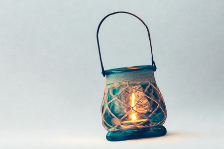 A teal glass lantern with a woven rope detail, illuminated by a warm, flickering candle, set against...