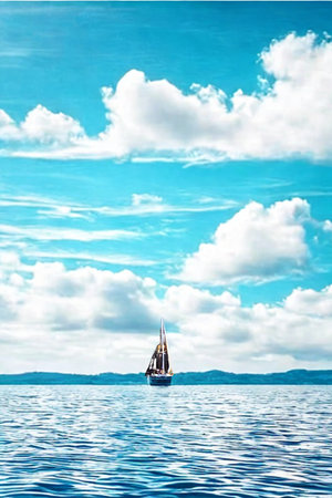 A lone sailboat navigates the calm, blue ocean waters beneath a sky filled with bright white clouds and vibrant blue.の写真素材