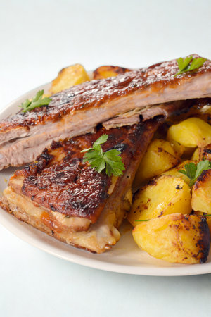 A close-up shot of succulent grilled pork ribs piled high on a plate with crispy, golden fried potatoes and fresh parsley garnish.の写真素材