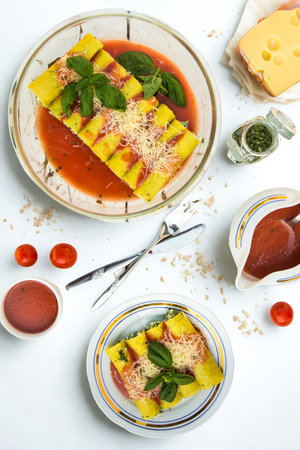 A close-up overhead view of a plate of fresh pasta with a vibrant tomato sauce and green herbs, garnished with cheese.の写真素材