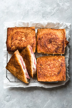 Four golden brown toasted sandwiches, two cut into triangles, are arranged on a wire cooling rack over parchment paper.の写真素材