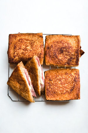 Four golden brown toasted bread slices, two rectangular and two triangular, arranged on a wire cooling rack against a white background.の写真素材