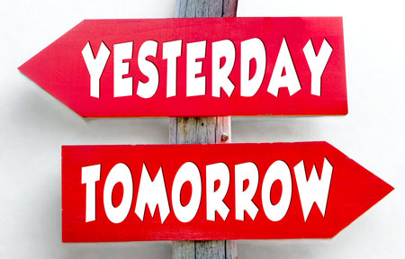 Two red arrow-shaped signs mounted vertically. The top sign reads Yesterday pointing left, and the bottom sign reads Tomorrow pointing right.の写真素材