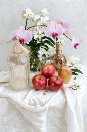 A still life arrangement featuring red apples orchids a decorative jar and a small figurine on a draped white cloth.の写真素材