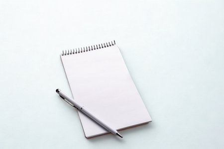 A clean, open spiral-bound notebook with blank pages and a pen resting on it, set against a bright white surface.の写真素材