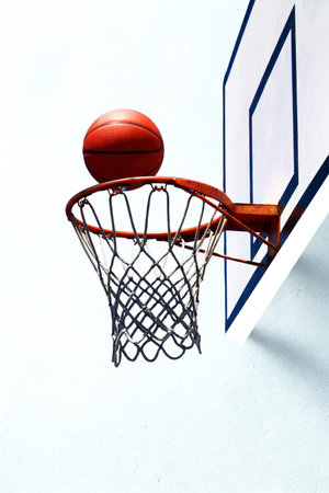 A close-up shot of a basketball teetering on the edge of a basketball hoop, with a white background.の写真素材