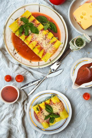 A close-up overhead view of a plate of cannelloni pasta, topped with fresh basil and a rich tomato sauce, served with side dishes.の写真素材