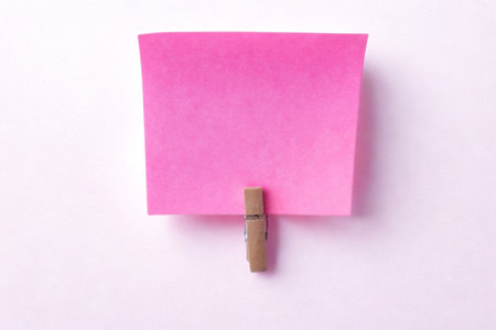 A single, vibrant pink sticky note is held to a white surface by a small wooden clothespin, casting a subtle shadow.の写真素材