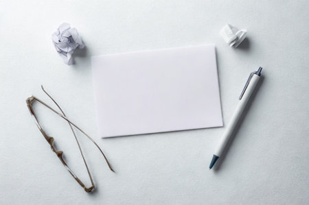 A flat lay composition featuring a blank white note card, a silver pen, crumpled paper balls on a pale background.の写真素材