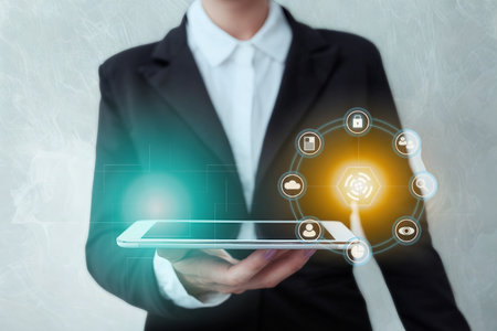 A person in a suit holds a tablet displaying a glowing digital interface with interconnected icons representing various business and technology concepts.の写真素材