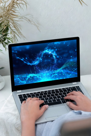 Close-up of hands typing on a laptop keyboard. The screen displays a bright, abstract blue pattern.の写真素材