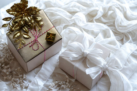 Two beautifully wrapped gift boxes adorned with luxurious gold and white ribbons, resting on a soft, flowing white fabric.の写真素材