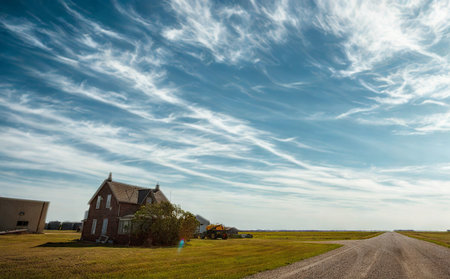 An old, weathered house stands alone in a vast, grassy field under a sky with wispy clouds.の写真素材