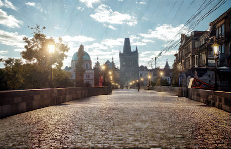 A sun-drenched cobblestone path winds towards a grand European city. Historic architecture and illuminated windows create a warm, inviting atmosphere.の写真素材
