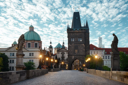 The historic Charles Bridge in Prague, Czech Republic, is illuminated by streetlights under a dramatic cloudy sky at sunrise.の写真素材
