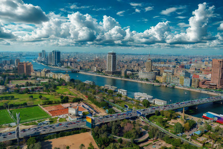 An aerial view of a sprawling city with a wide river cutting through it, under a sky filled with dramatic clouds.の写真素材