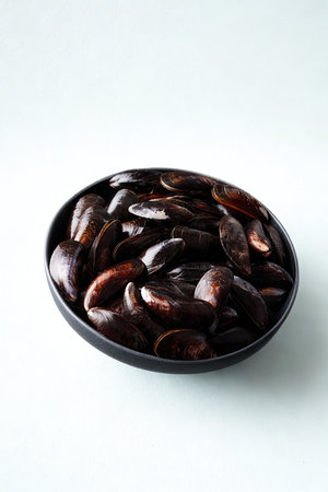 A dark, oval bowl is filled with many shiny, plump, dark brown dates against a white background.の写真素材