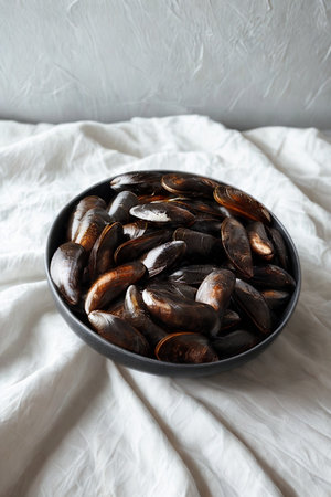 A dark oval platter overflows with plump, shiny dates, resting on a rumpled white linen cloth with a soft gray background.の写真素材