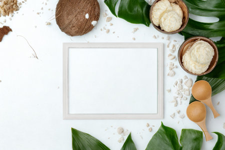 A flat lay composition featuring coconut halves, green leaves, and eggs surrounding a blank white frame, ideal for natural product branding.の写真素材