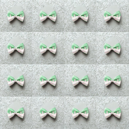 A grid of sixteen identical mint green and white ribbon bows are evenly spaced on a light blue textured surface.の写真素材