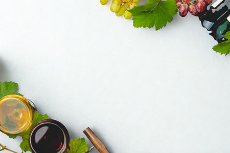 A top-down view of grapes, wine bottles, and a glass of red wine arranged on a clean white surface with ample copy space.の写真素材