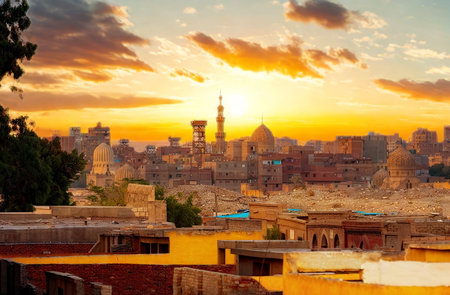 A vibrant sunset casts a warm golden glow over an ancient city, highlighting its buildings and a prominent minaret.の写真素材