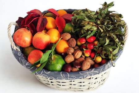 A woven basket overflows with a vibrant mix of fruits, nuts, and dried autumn foliage, creating a rich display of seasonal bounty.の写真素材