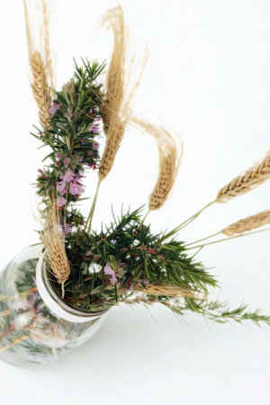 A rustic arrangement of dried wildflowers and grasses spills from a glass jar against a bright white background.の写真素材