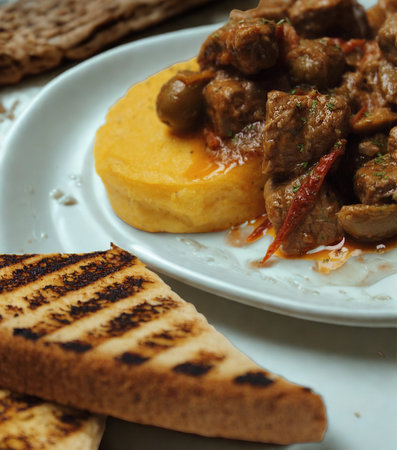 A close-up of a plate featuring tender beef stew atop creamy polenta, accompanied by slices of grilled bread.の写真素材