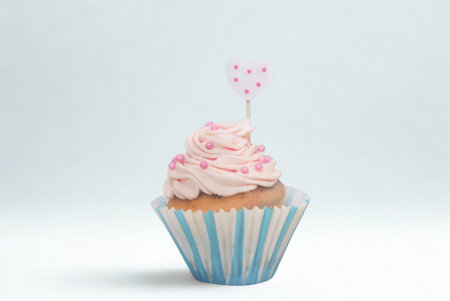 A single, delicious cupcake with swirled pink frosting and a small decorative flag sits in a striped wrapper against a plain background.の写真素材