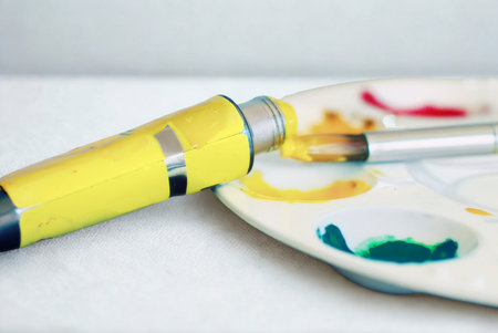 A yellow paint tube rests on a palette with dabs of red, yellow, and green paint, ready for artistic creation.の写真素材