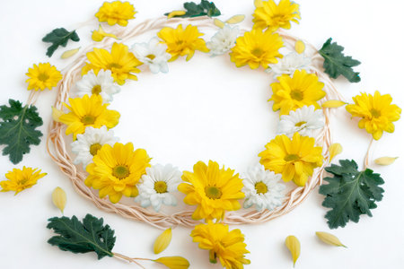 A delicate circular wreath made of bright yellow and white flowers, accented with dark green leaves on a white background.の写真素材