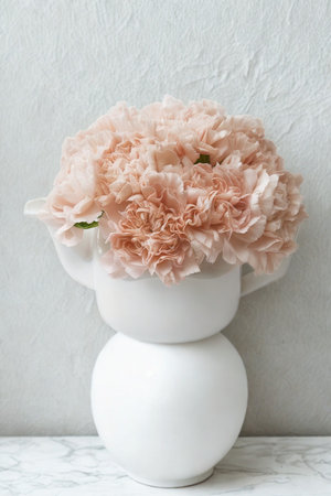 A delicate bouquet of pink and peach flowers is artfully arranged in a minimalist, two-tiered white ceramic vase against a textured backdrop.の写真素材