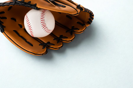 A baseball rests snugly in a worn leather baseball glove, poised for action on a clean, light background.の写真素材