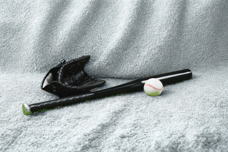 A baseball bat, glove, and ball are arranged on a soft, textured surface, suggesting a moment of rest or preparation.の写真素材