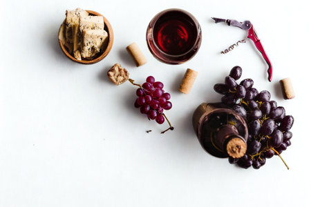 A top-down view of red wine, grapes, walnuts, corks, and a corkscrew arranged on a white surface.の写真素材