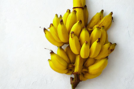 A vibrant bunch of ripe yellow bananas hangs from a stem against a clean white backdrop, showcasing their natural texture and color.の写真素材