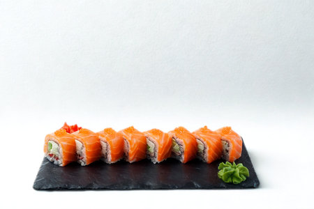 A row of vibrant salmon sushi rolls, filled with creamy ingredients, is presented on a dark slate plate with a dollop of green wasabi.の写真素材