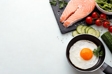 A top-down view of a raw salmon fillet, a fried egg in a pan, and fresh vegetables, suggesting a healthy and delicious meal preparation.の写真素材