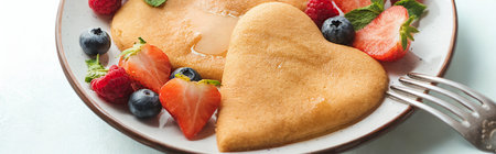 A close-up of heart-shaped pancakes served with fresh strawberries and blueberries, ready to be eaten with a fork.の写真素材