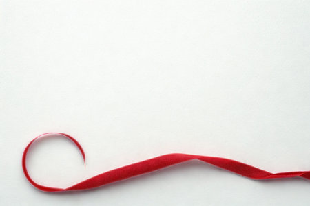 A single, flowing red ribbon with a subtle sparkle is elegantly curled against a clean white backdrop.の写真素材
