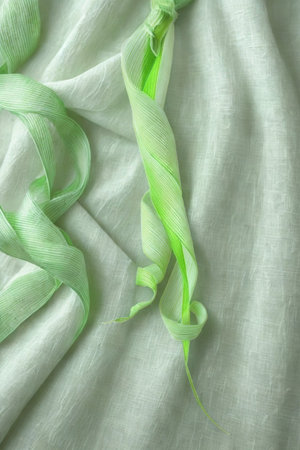 A close-up shot of a textured fabric with a light green ribbon woven through it, creating a gentle and artistic effect.の写真素材