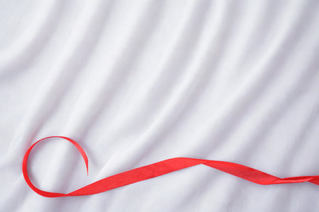 A single red ribbon gracefully curves across a soft, white, draped fabric surface, creating a minimalist and elegant composition.の写真素材