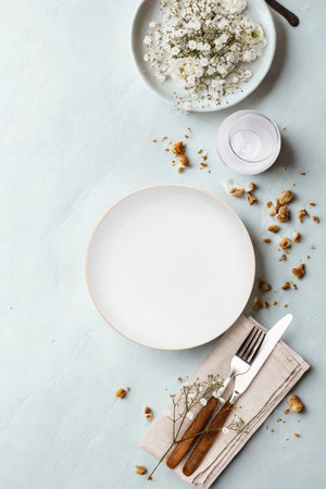 A clean white plate sits on a light blue surface, ready for a meal. Crumbs and cutlery are artfully arranged nearby.の写真素材